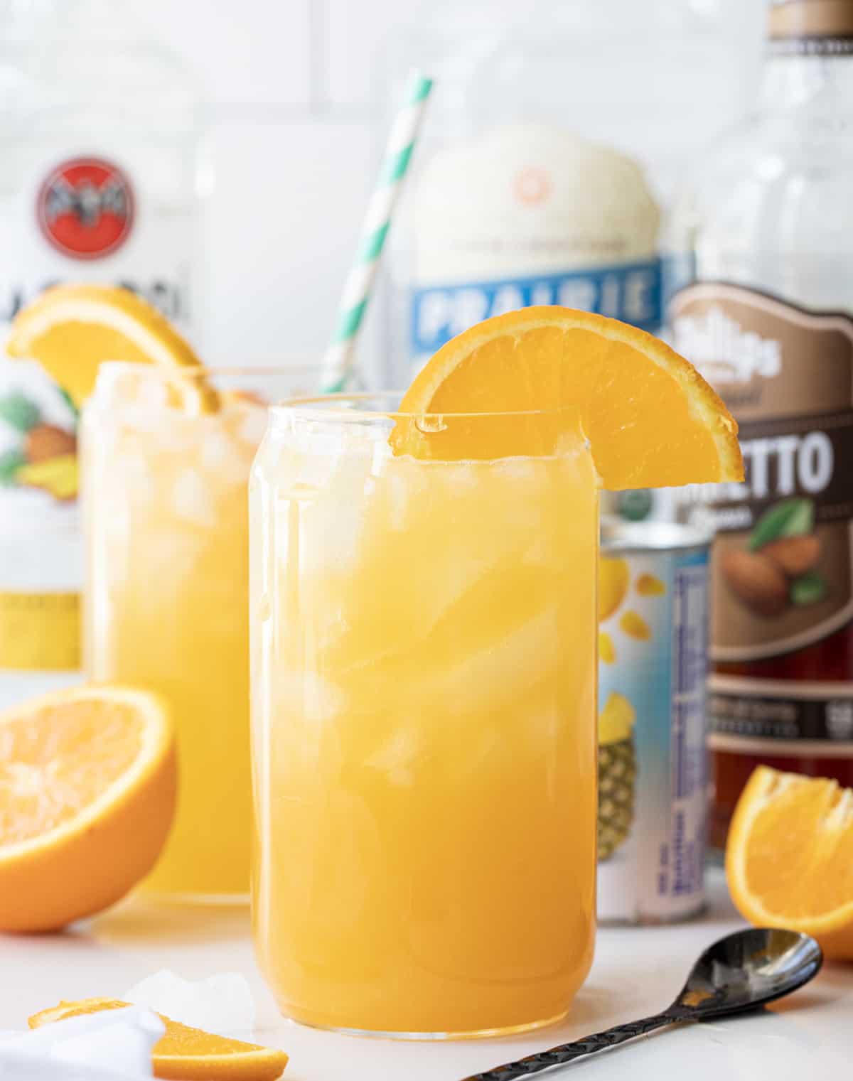 Yellow Hammer Slammer is an adult cocktail made with vodka, pineapple rum, amaretto, orange juice, and pineapple juice. It's a refreshing drink that is based on a cocktail that was created in Gallettes bar in Tuscaloosa, Alabama. It's their signature drink (Yellow Hammer) that is most popular on game day, meaning Alabama football games. But, you can recreate the drink at home, no need to wait for football season! Glass of Yellow Hammer Slammer in Front of All The Liquors That Go Into It.